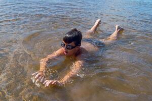 A boy swims energetically in a serene lake while wearing goggles photo