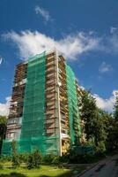 A tall building is under renovation with green netting covering its sides photo