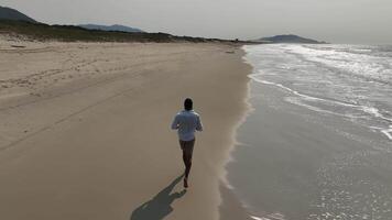 Man walking and running on sand dunes near the beach. Aerial image with drone following the man. Image from above. Health concept. video