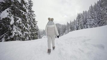 Woman dressed in white walks on path full of snow in the forest video