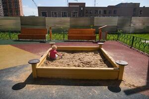 Child playing in the sandbox in the playground in the courtyard of a house photo