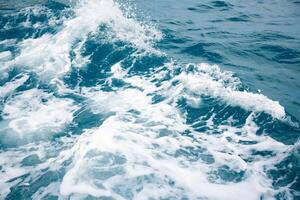 Wave on blue water and white foam on the tops of the waves from under the side of a floating boat, space for text photo
