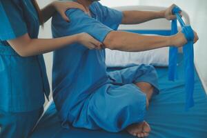 Close up hand patient doing stretching exercise with a flexible exercise band and a physical therapist hand to help in clinic room. photo