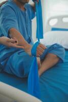 Close up hand patient doing stretching exercise with a flexible exercise band and a physical therapist hand to help in clinic room. photo