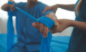 Close up hand patient doing stretching exercise with a flexible exercise band and a physical therapist hand to help in clinic room. photo