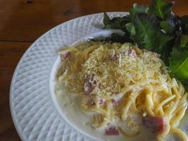 Spaghetti carbonara in a white plate on a wooden table at a restaurant photo