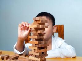 Cheerful Asian boy playing with wooden building blocks Jenga, Having fun and learning creativity, smart kid concept, wooden block Planning, Risk and strategy of project management in business. photo