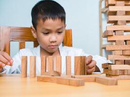Cheerful Asian boy playing with wooden building blocks Jenga, Having fun and learning creativity, smart kid concept, wooden block Planning, Risk and strategy of project management in business. photo