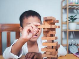 Cheerful Asian boy playing with wooden building blocks Jenga, Having fun and learning creativity, smart kid concept, wooden block Planning, Risk and strategy of project management in business. photo