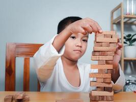 Cheerful Asian boy playing with wooden building blocks Jenga, Having fun and learning creativity, smart kid concept, wooden block Planning, Risk and strategy of project management in business. photo