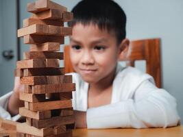 Cheerful Asian boy playing with wooden building blocks Jenga, Having fun and learning creativity, smart kid concept, wooden block Planning, Risk and strategy of project management in business. photo