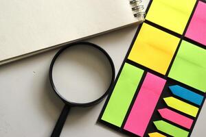flat lay of notepad and magnifying glass and colorful sticky notes on white background photo