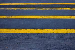 Closeup of a textured asphalt road with weathered yellow stripes on a rough gray pavement, great for use in street photography, urban design, or traffic-related visuals. Copy space photo