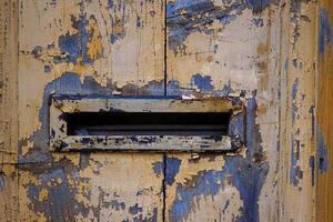 Closeup image of a weathered, peeling paint on an old wooden door with a vintage mail slot, perfect for backgrounds, textures, and rustic-themed designs. Copy space photo