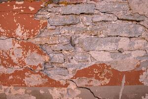 Cracked wall with rustic charm. A detailed close-up of a weathered wall with peeling red paint, revealing layers of plaster and brick underneath. Copy space photo