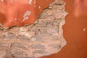 Cracked wall with rustic charm. A detailed close-up of a weathered wall with peeling red paint, revealing layers of plaster and brick underneath. Copy space photo