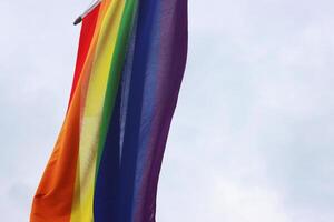 Fragment of the rainbow flag, a symbol for the LGBT community, hanging waving in the wind with a cloudy sky background photo