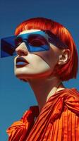 Captivating Redhead Model in Vibrant Orange Outfit and Futuristic Sunglasses Against Blue Background photo