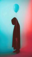 Hooded figure silhouette floating with a blue balloon in a minimalist surreal scene photo