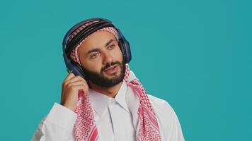 Groovy man dancing on camera, listening to modern tunes on headset and having fun in studio. Middle eastern man in traditional attire showing funky dance moves and singing songs. photo