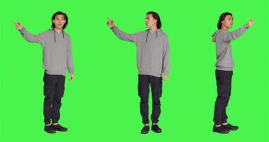 Model showing left or right directions in studio, pointing to both sides and indicating another path. Asian young adult advising someone to go that way, full body greenscreen backdrop. photo