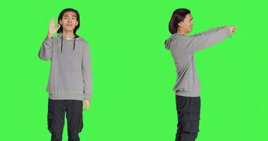 Person doing okay sign and showing disapproval at the same time, expressing positivity and negativity over greenscreen isolated backdrop. Young man presenting good and bad sign. photo