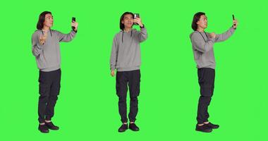 Asian person on videocall network with friends, using smartphone to call friends using phone camera against greenscreen. Male adult talking to people on videoconference connection. photo