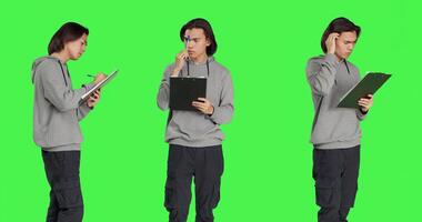 Young man taking notes and thinking about ideas to write on clipboard papers, using files for inspiration in studio. Adult being thoughtful and in doubt, writing information on camera. photo