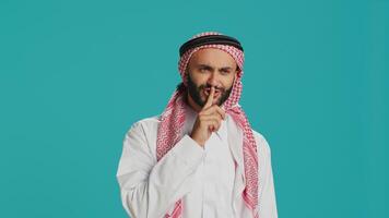 Arabic adult showing silence symbol with finger over lips, presenting hush mute sign on camera. Private person doing confidential secrecy gesture in studio, trying to keep secret. photo