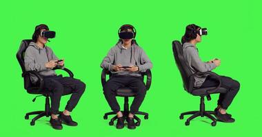 Gamer using vr interactive headset and smartphone to play online mobile games, sitting on chair over full body greenscreen backdrop. Skilled person playing fun multiplayer action videogames. photo