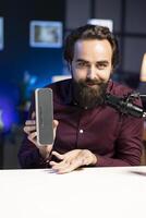 Cheerful online star doing technology review of Bluetooth portable speaker for online platforms channel. Joyful influencer showcasing music playing device to his viewership photo