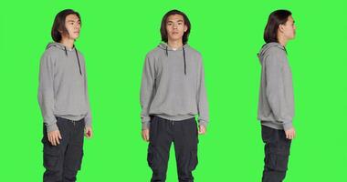 Asian friendly model standing in studio and posing with confidence, smiling against isolated greenscreen background. Young adult acting optimistic and relaxed in casual jeans. photo