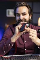 Portrait of cheerful influencer filming for online channel in apartment studio, presenting gaming mouse to audience. Joyful man showing viewers computer peripheral device, recommending it photo