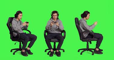 Asian person playing mobile games over full body greenscreen, holding smartphone to play online rpg contest. Modern gamer using phone gadget to have fun with new gameplay on chair. photo