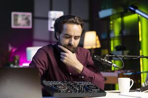 Artist filming DJ mixing tutorial, thinking of examples of sampling on sound controller to teach audience. Man contemplating if mixer musical equipment deserves endorsement photo