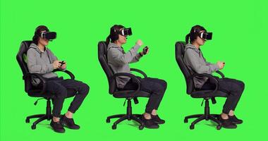 Asian man wears virtual reality headset on greenscreen set, enjoying web games with gaming controller. Young adult having fun with rpg competition and vr modern headset. photo