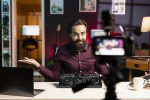 Artist filming DJ mixing tutorial using professional camera, showing fans examples of sampling on sound controller. Man presenting settings on turntables mixer, recording with high tech gear photo