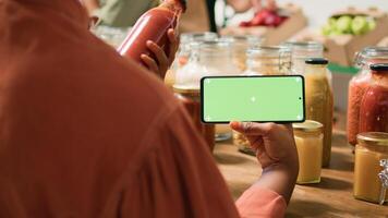 African american woman shows greenscreen looking at organic natural bulk products placed in reusable jars. Customer checks smartphone app with isolated chromakey display. photo