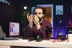 Influencer filming for online channel in home studio, presenting wired gaming mouse to audience. Content creator showing viewers computer peripheral device, carefully analyzing it photo