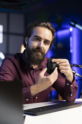 Smiling tech expert filming review for online channel in apartment studio, analyzing office mouse for audience. Happy content creator recommending computer peripheral device