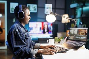 Black woman immersed in world of technology, wearing wireless headphones as she edits photos and videos. African american female filmmaker working with footage and sound, editing new project.