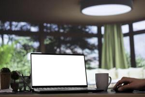 Billionaire business leader uses white screen on laptop at his impressive mountain cabin, viewing pc projection of blank copyspace display. Company CEO interacts with isolated mockup layout. photo