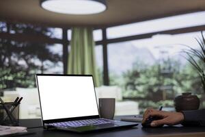 Rich industrialist works from his posh alpine villa in the forest, examining white isolated display on laptop. Entrepreneur uses computer to check blank mockup screen, high end lifestyle. photo