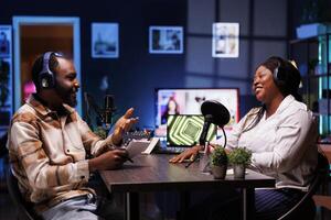 Podcasters enjoying happy conversations with online listeners in home studio, covering wide range of subjects. Man carrying notebook is speaking with socialite and they are having a good discussion. photo