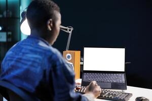 Black woman using a laptop displaying isolated white screen. African american freelancer typing on keyboard while her personal computer displays blank chromakey copyspace template. photo