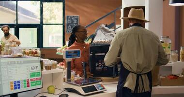 Seller preparing groceries order for home delivery, putting organic produce in backpack. African american employee coming to pick up fruits and vegetables for local eco store customers. photo