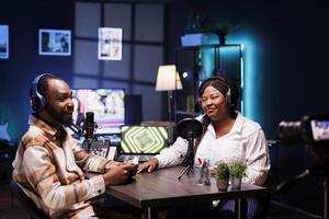 Cheerful media stars recording a podcast in home studio with professional filming equipment for broadcast on live streaming platform. Blogger interviewing celebrity, filming the encounter with camera. photo