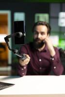 Focus on smartphone on selfie stick used by ASMR creator in blurry background to do anti stress for viewers. Close up on professional microphone used by man doing relaxing ambient sounds photo