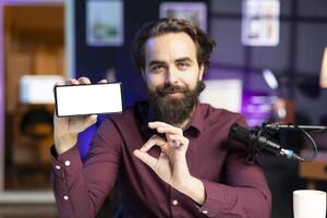 Man holding isolated screen smartphone in hand, using it as empty copy space to showcase his online streaming channel logo. Content creator does introductory using mockup mobile phone photo