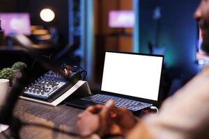 Electronic device near microphone audio mixer is displaying an isolated white screen. Digital laptop on table is showing a blank copyspace mockup template for podcast show advertisement. photo
